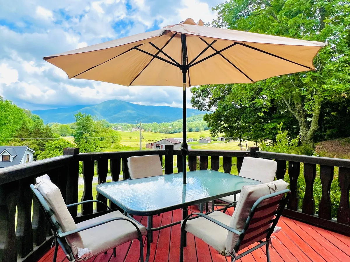 An inviting outdoor deck with a glass-top table, parasol, and stunning mountain views beyond the railing. The space suggests outdoor dining, relaxation, and shared family moments surrounded by nature.