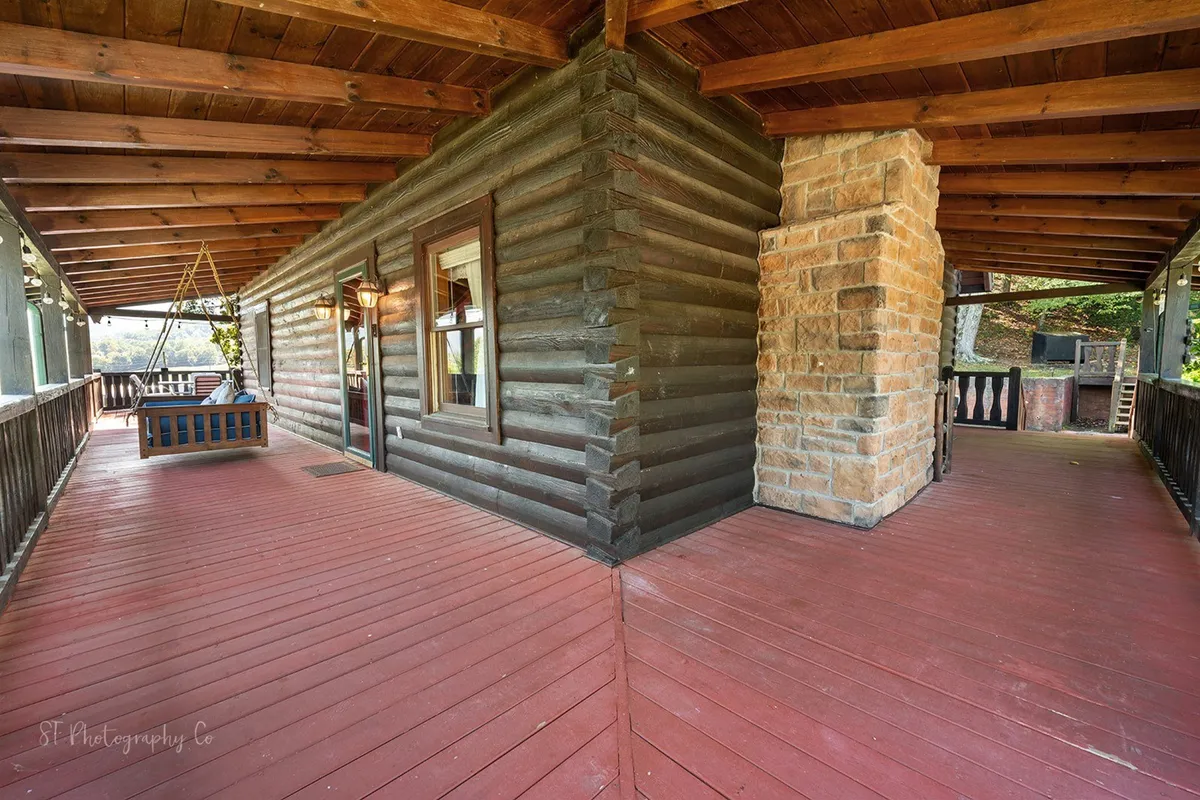 A charming log cabin porch with a swinging bench and a stone fireplace, set in a lush natural environment. The inviting porch encourages guests to relax, socialize, and enjoy the peaceful mountain surroundings.