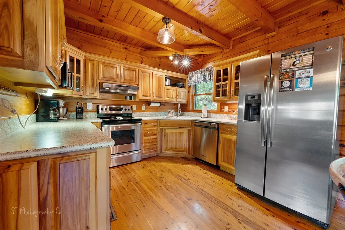 The image showcases a warm, inviting kitchen featuring stainless steel appliances, a spacious kitchen island, wooden cabinetry, and granite countertops. The lighting and layout suggest a space designed for both efficiency and togetherness, with visible areas for cooking and gathering.
