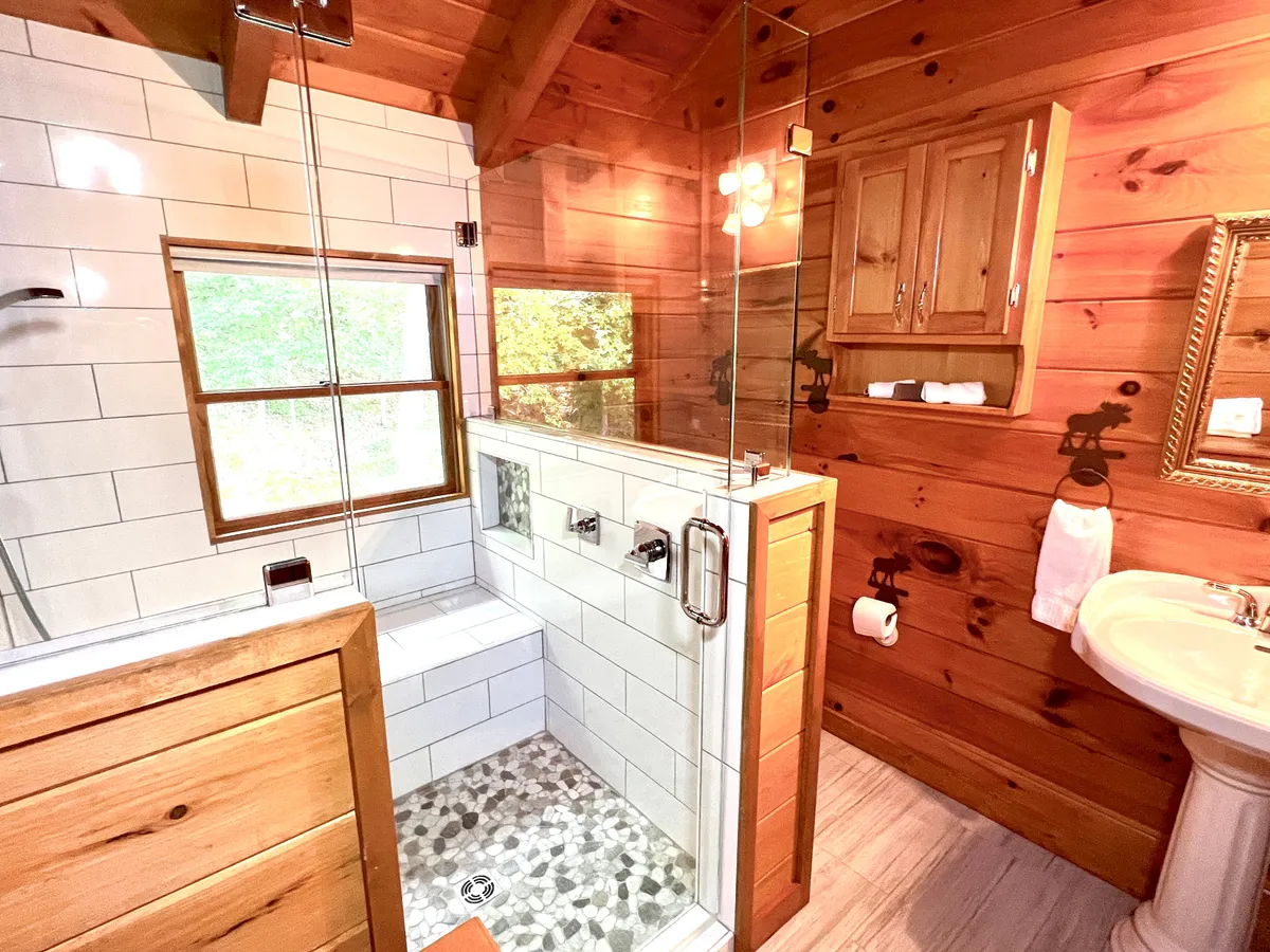 A well-lit bathroom with a glass shower enclosure, wood cabinetry, and natural light pouring in from the window. The space feels serene and spa-like—ideal for refreshing after a day outdoors.