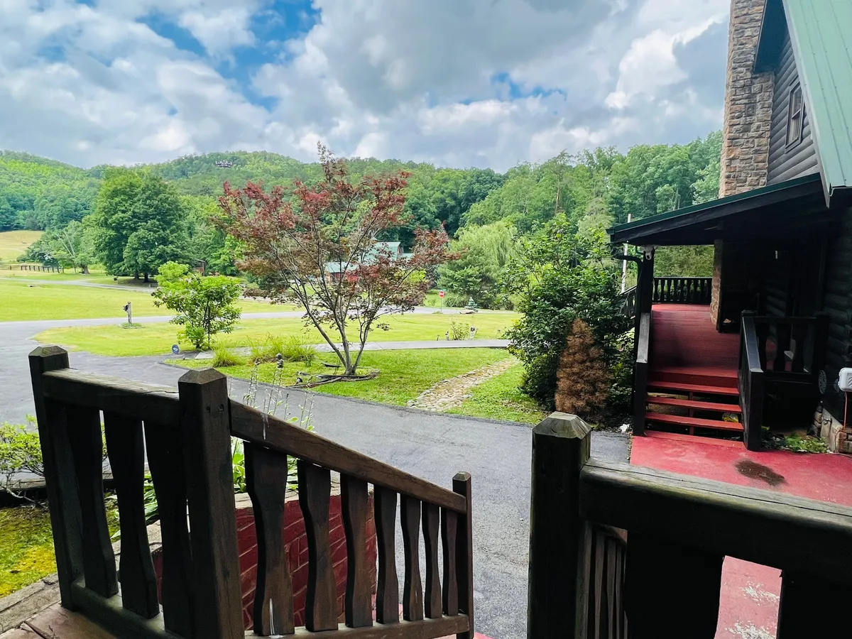 A wooden staircase leads through lush greenery with a majestic mountain backdrop and a stone building nestled in the landscape. The scene radiates serenity and adventure, ideal for morning walks, exploring nearby trails, or enjoying nature with a pet.