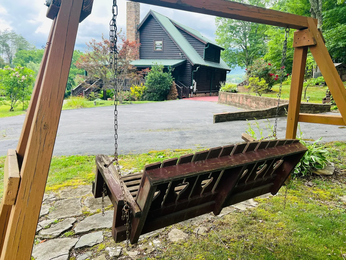 A closeup exterior of the log cabin-style house featuring a wooden swing on the porch, surrounded by lush greenery. The swing and porch set a relaxing tone, ideal for unwinding after a busy day of exploring local attractions.